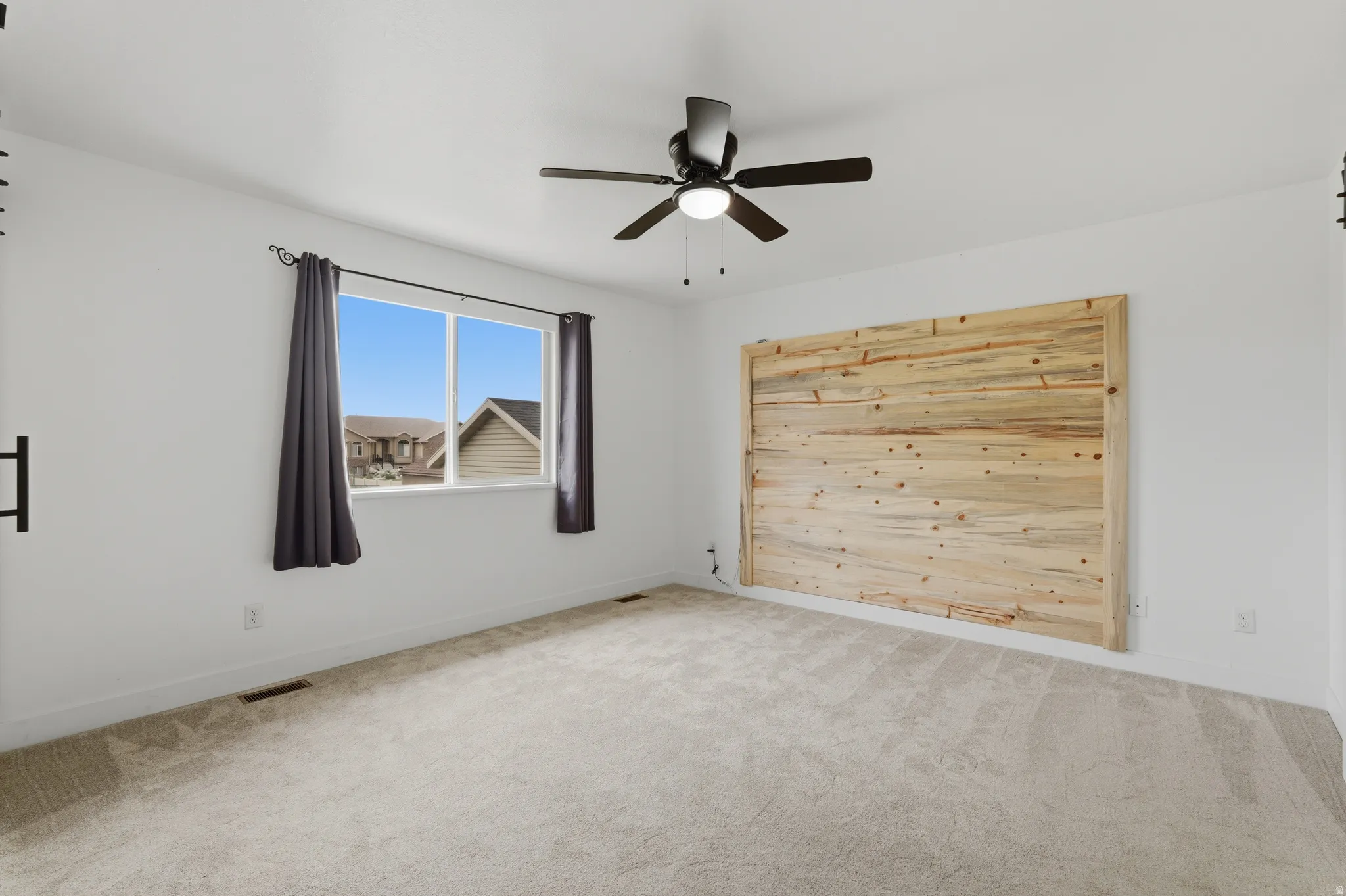 Spacious room featuring light-toned carpet flooring, a large window, and a ceiling fan with integrated lighting
