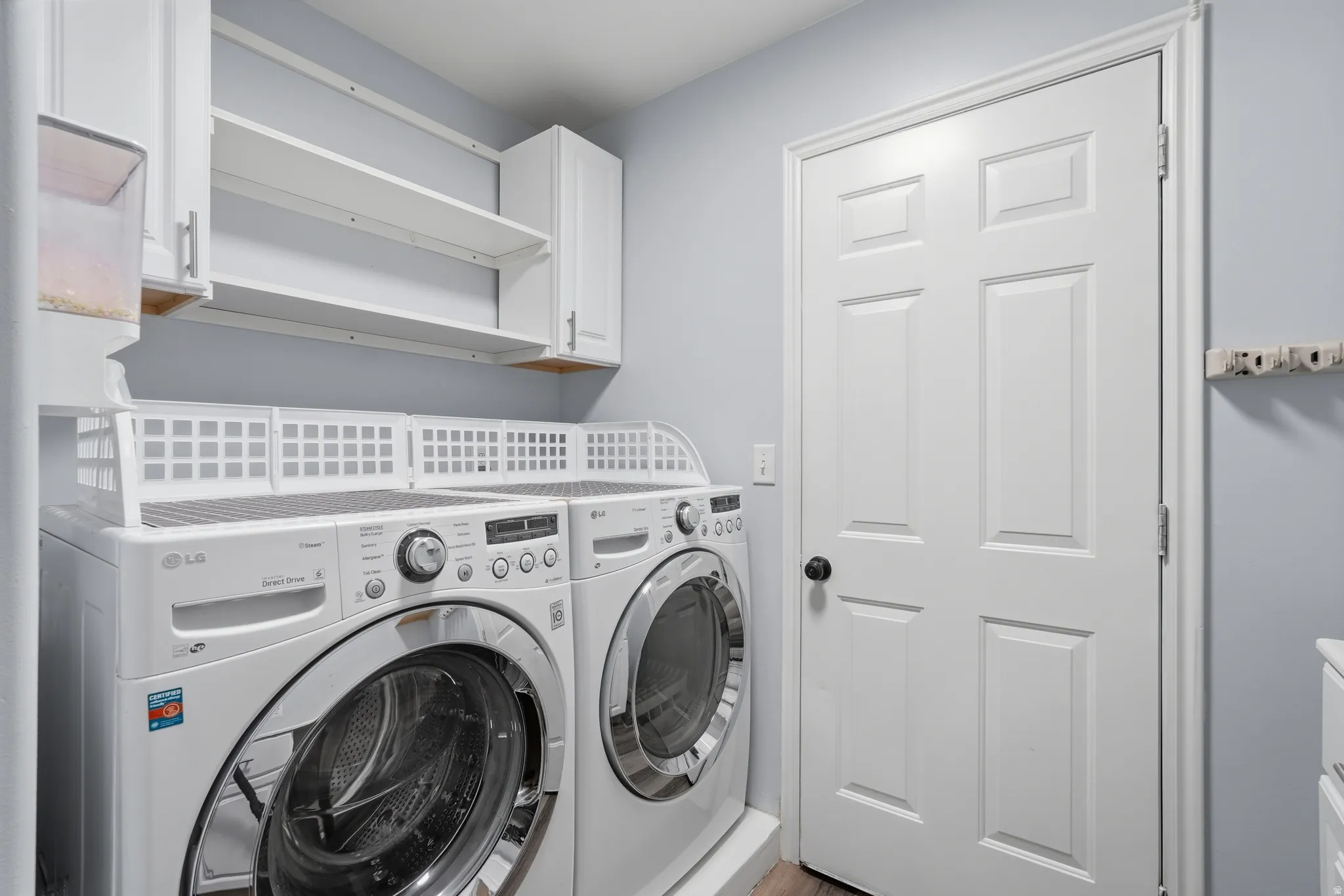 Laundry area featuring built-in cabinetry, open shelving, and wood-finish flooring