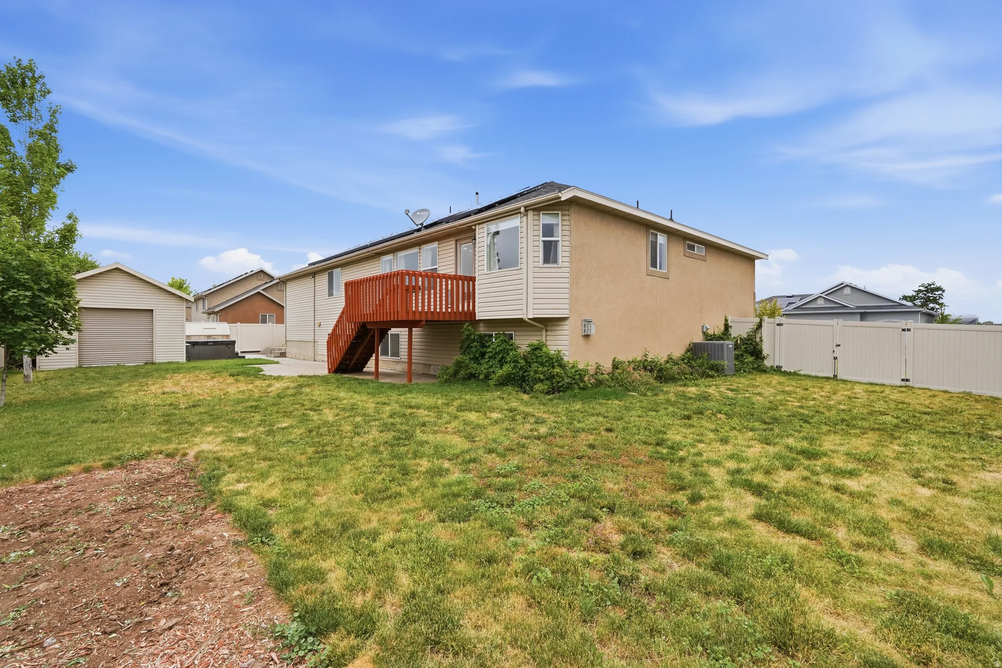 Expansive backyard featuring a concrete patio, a detached two-car garage with a roll-up door, a privacy fence, and an upper-level deck with stairs