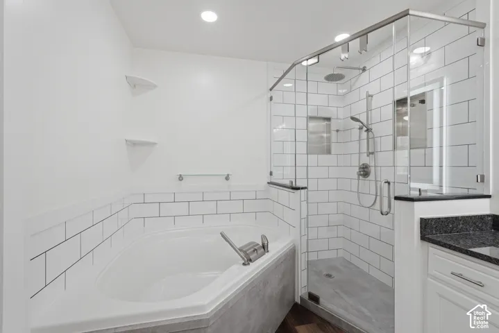 Contemporary bathroom featuring a corner soaking tub, a frameless glass shower with subway tile surround, a built-in shower niche, and a vanity with a dark countertop
