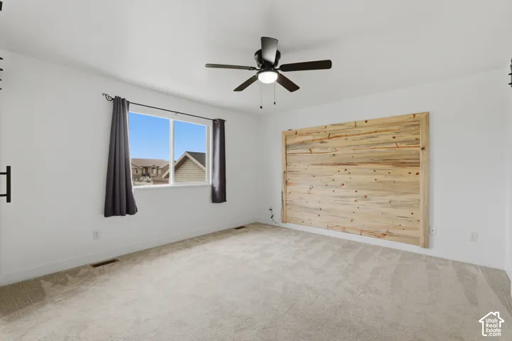 Spacious room featuring light-toned carpet flooring, a large window, and a ceiling fan with integrated lighting