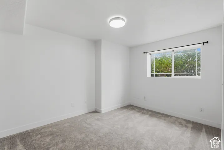 Spacious room featuring light gray carpeting, crisp white walls, a contemporary flush-mount ceiling light, and a large window with black curtain rods