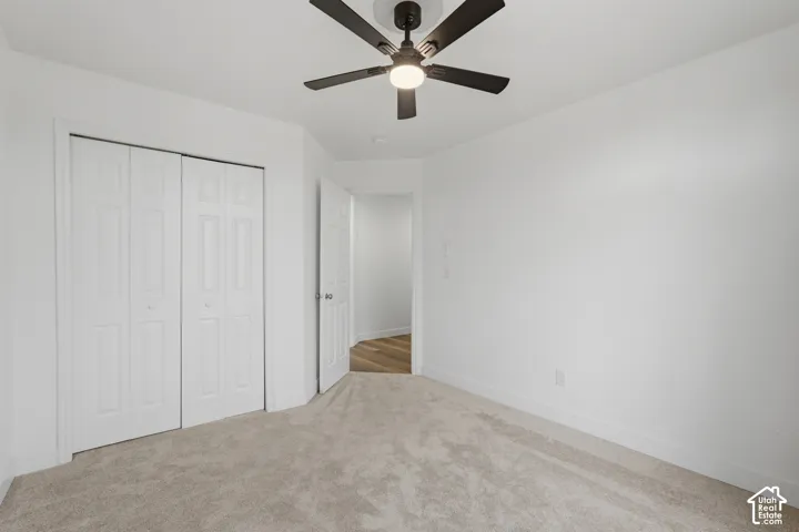 Carpeted room with white walls, bi-fold closet doors, a ceiling fan with integrated lighting, and white baseboards