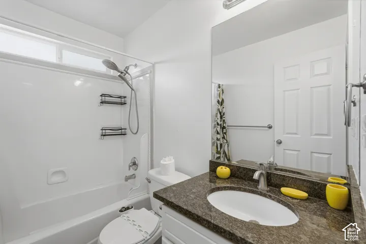 Bathroom featuring a shower-over-tub combination with a handheld showerhead, a high-set window, and a white vanity with a dark speckled countertop and undermount sink
