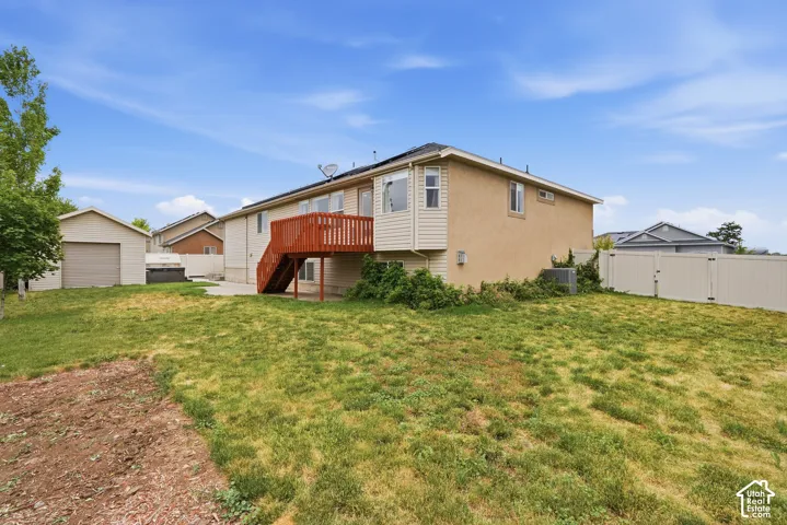 Expansive backyard featuring a concrete patio, a detached two-car garage with a roll-up door, a privacy fence, and an upper-level deck with stairs