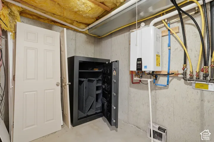 Utility area featuring a tankless water heater, exposed concrete foundation walls, and visible ceiling insulation