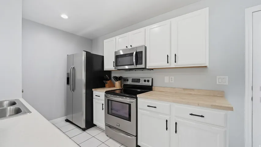 Kitchen featuring white cabinetry with matte black hardware, stainless steel appliances, wood-finish countertops, and white tile flooring