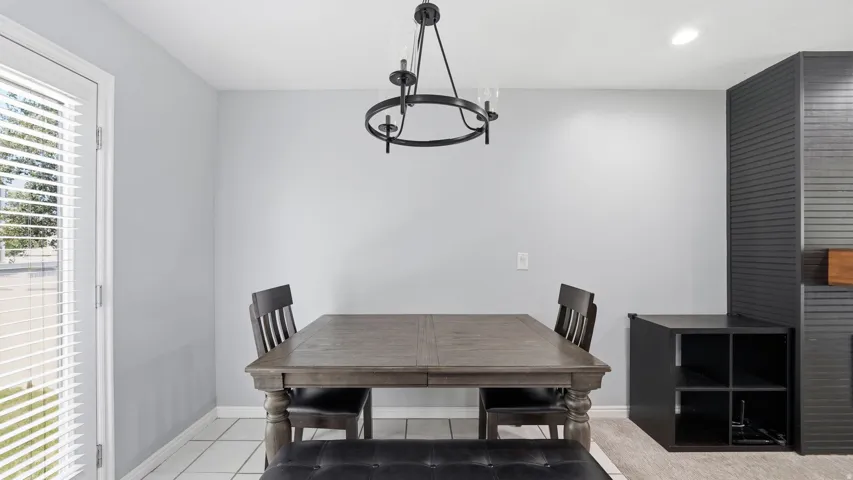 Bright room featuring a glass-paned door with blinds, white square floor tiles, and a contemporary chandelier