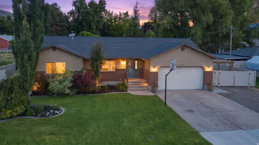 Ranch-style residence featuring a prominent front lawn, mature landscaping, an attached two-car garage, and a concrete driveway