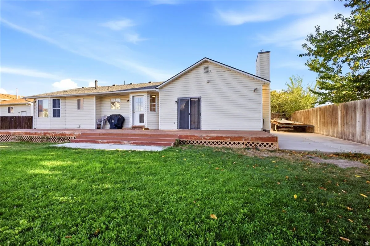 Expansive lawn with a multi-level wood deck, white vinyl siding, and a privacy fence