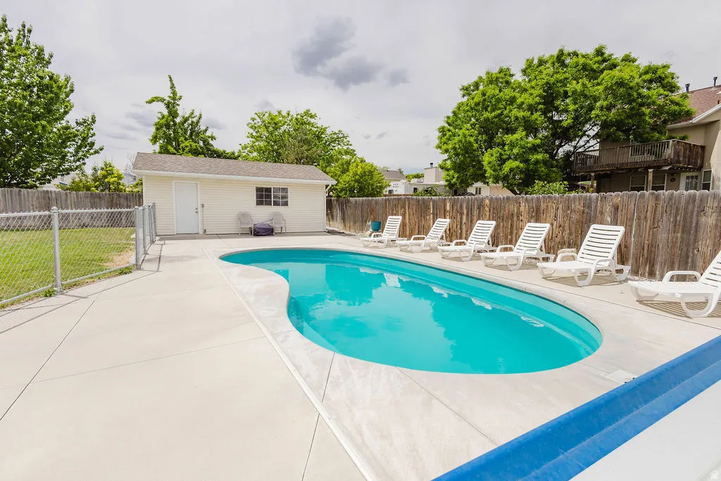 Outdoor swimming pool with concrete surround, wood privacy fencing, and a separate storage shed