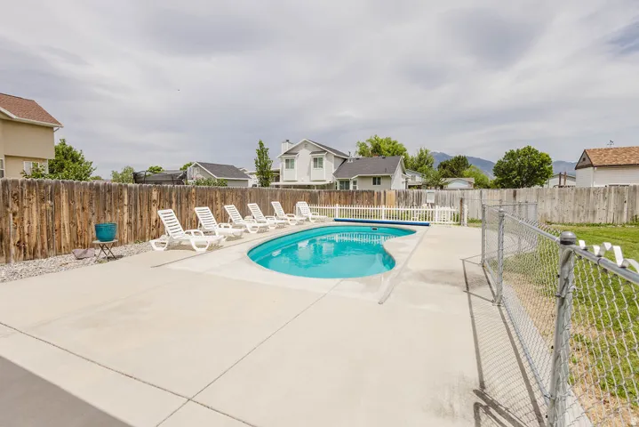 Outdoor swimming pool with a concrete surround, wood privacy fencing, and a separate chain link enclosure