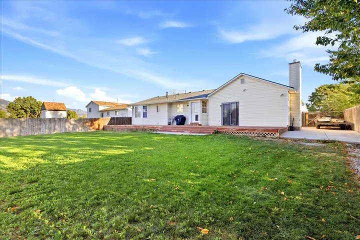 Expansive grassy yard with a wood fence, leading to a rear deck and sliding glass door access