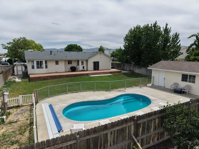 Rear exterior featuring an in-ground swimming pool with surrounding concrete patio, a spacious wood deck, a detached shed, and a privacy fence