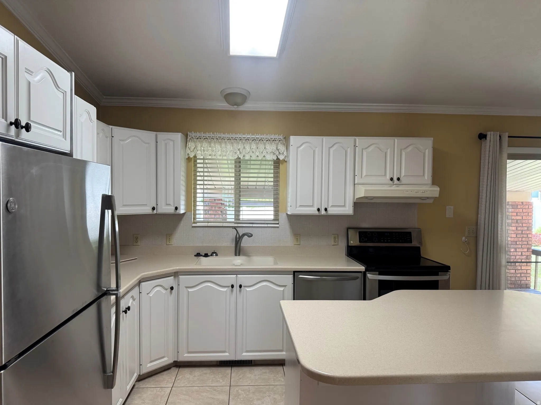 Kitchen featuring white cabinetry, light-toned countertops, tile flooring, and stainless steel appliances