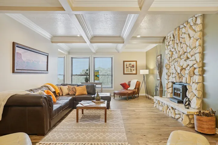 Living area featuring a stone-clad fireplace with hearth, wood-finish flooring, coffered ceiling, and multiple windows