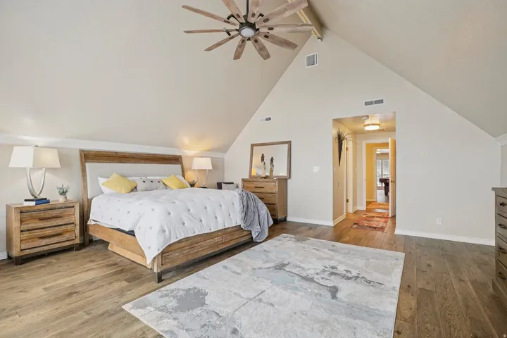 Vaulted ceiling bedroom featuring wood-finish flooring, a ceiling fan with light fixture, and a neutral color palette