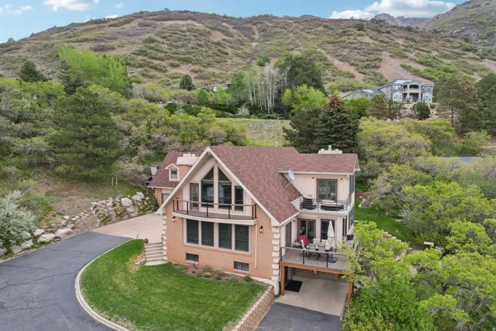 Hillside property featuring a multi-level design with a prominent gable window, multiple balconies with dark railings, a brick and stucco exterior, and a paved driveway with retaining walls
