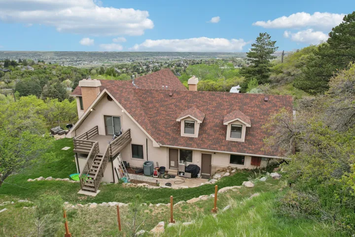 Multi-level residence featuring a brown shingle roof, twin dormer windows, and a large wooden deck with exterior stairs