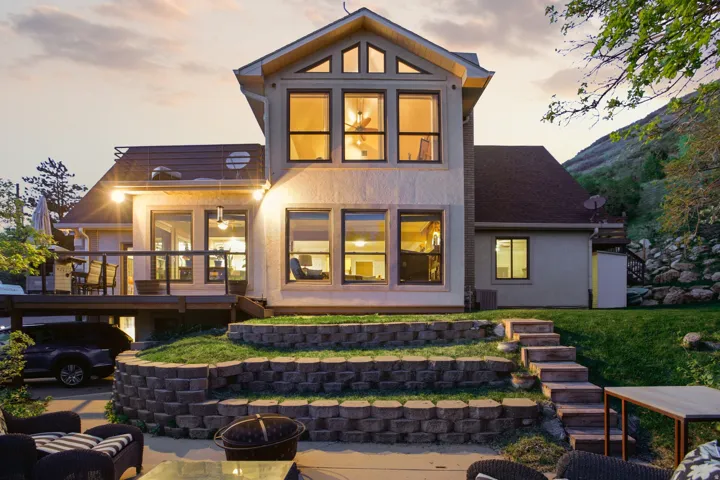 Multi-level stucco exterior featuring an upper deck, tiered retaining walls, a stone pathway, and extensive window placements