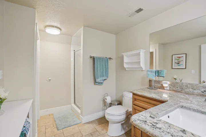 Bathroom featuring a glass-enclosed shower, a vanity with a light-toned stone countertop, an integrated sink, and wood-finish cabinetry