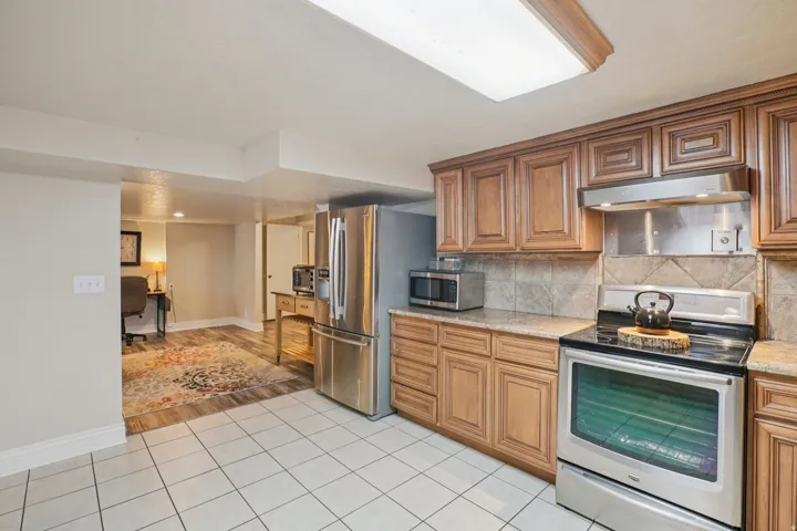 Kitchen featuring wood cabinetry, stainless steel appliances, tile flooring, and a tile backsplash