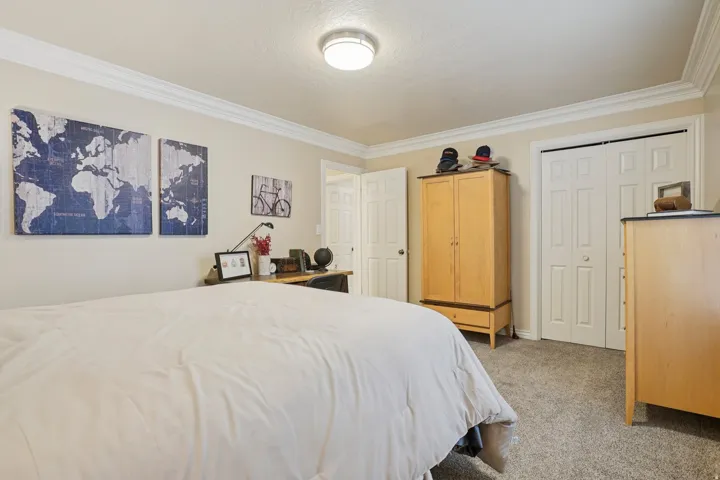 Carpeted bedroom featuring neutral-toned walls, crown molding, and a flush-mount ceiling light fixture
