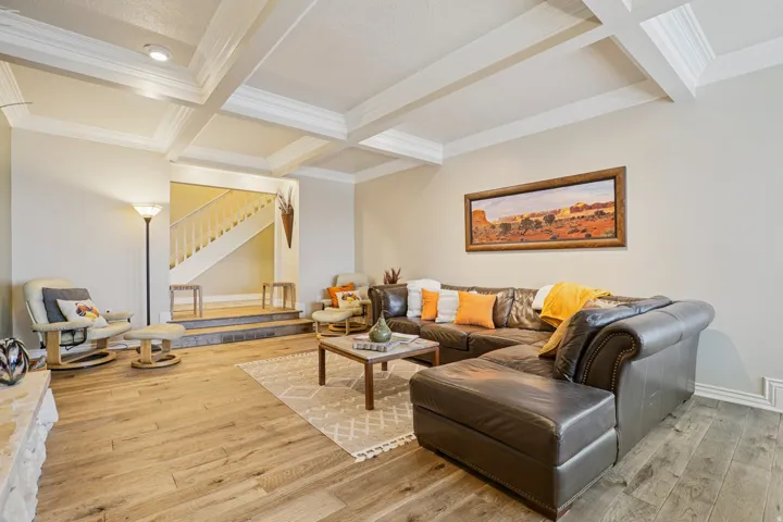 Spacious living area featuring wood-finish flooring, a coffered ceiling with recessed lighting, and a stone-faced hearth