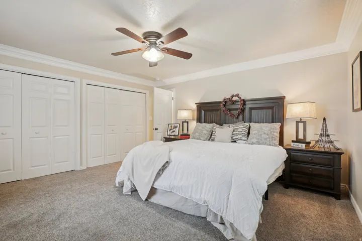 Bedroom featuring textured carpet flooring, a ceiling fan with integrated lighting, crown molding, and two bi-fold closet doors