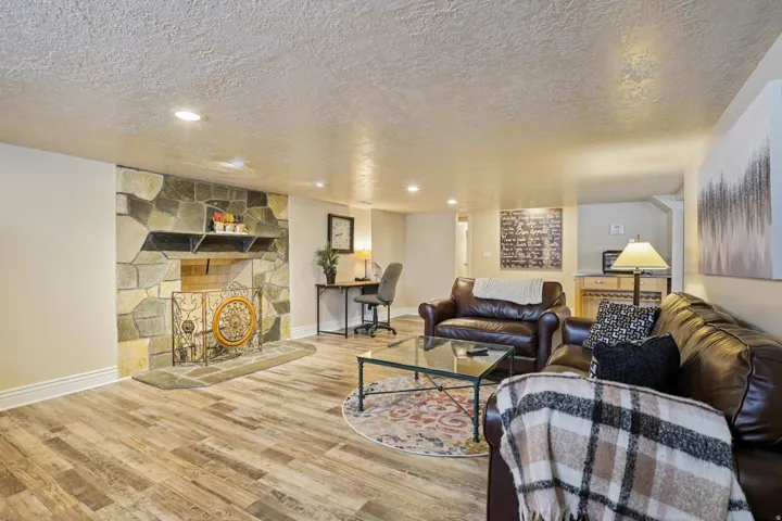 Living area featuring a stone accent wall fireplace, wood-finish flooring, recessed lighting, and a built-in wet bar with cabinetry