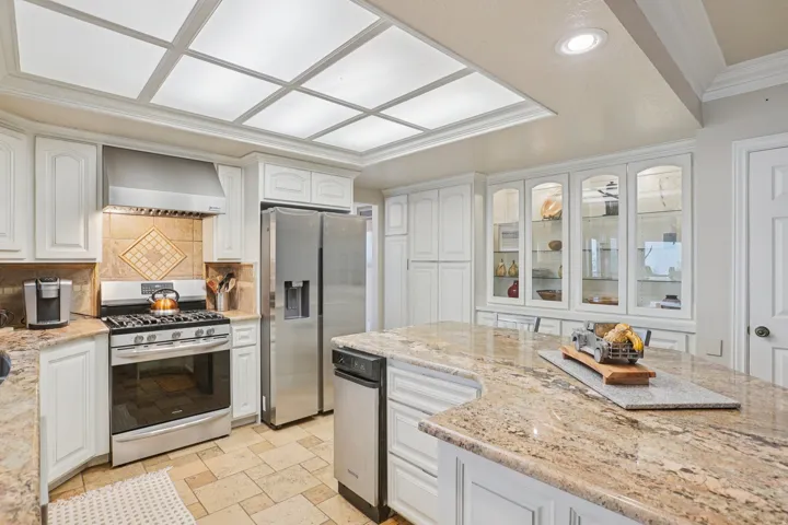 Spacious kitchen featuring an expansive island with a polished countertop, stainless steel appliances, white cabinetry, a tiled backsplash, and recessed lighting