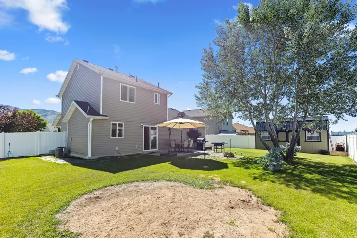 Spacious backyard featuring a manicured lawn, established trees, and a concrete patio