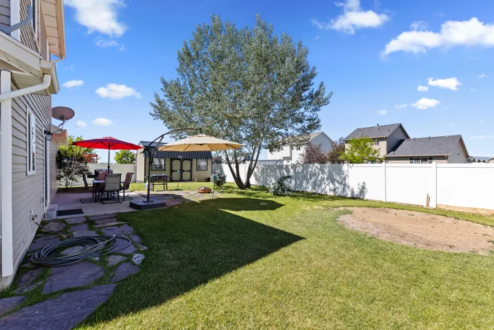 Expansive backyard featuring a manicured lawn, a large mature tree, a flagstone patio, a white privacy fence, and an outdoor storage shed