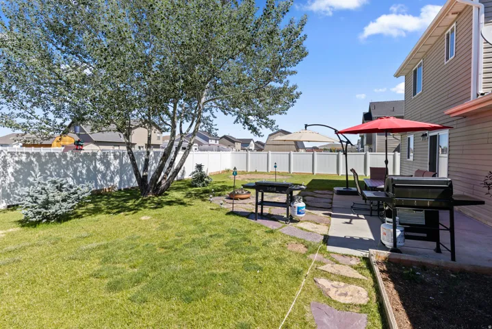 Expansive backyard featuring a mature deciduous tree, a white vinyl privacy fence, a concrete patio, and flagstone pavers