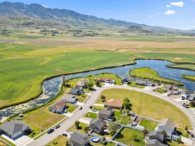 Aerial perspective showcasing a residential community with a large water feature, surrounded by expansive green fields and distant mountains