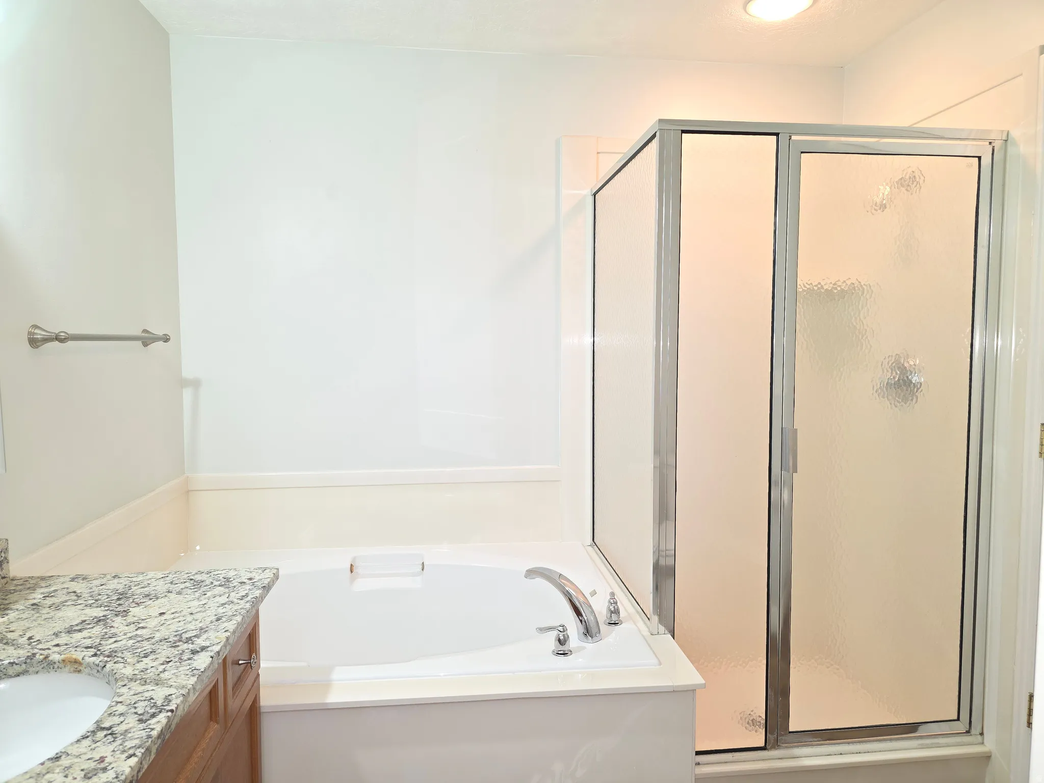 Bathroom featuring a built-in soaking tub, a separate glass-enclosed shower, and a vanity with a granite-style countertop and integrated sink