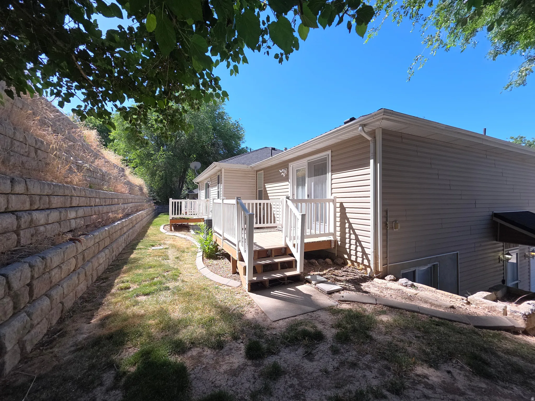 Backyard featuring a tiered block retaining wall, a wood deck with white railings, and a sliding glass door
