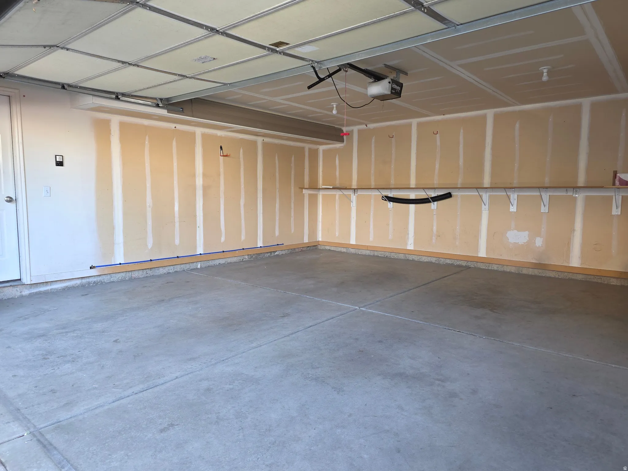 Spacious garage featuring a concrete floor, overhead garage door with opener, interior access door, and wall-mounted shelving brackets