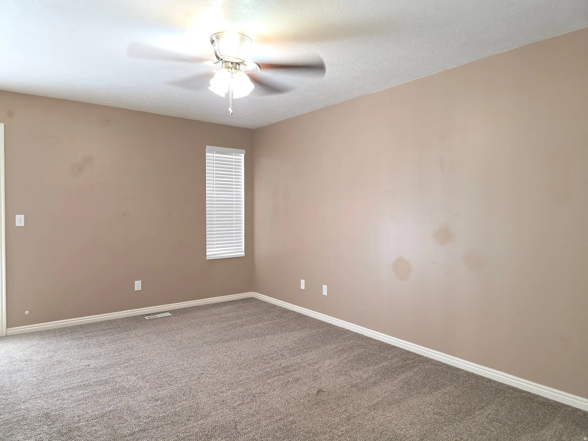 Carpeted room featuring a ceiling fan with light fixture, a single window with horizontal blinds, and neutral-toned walls