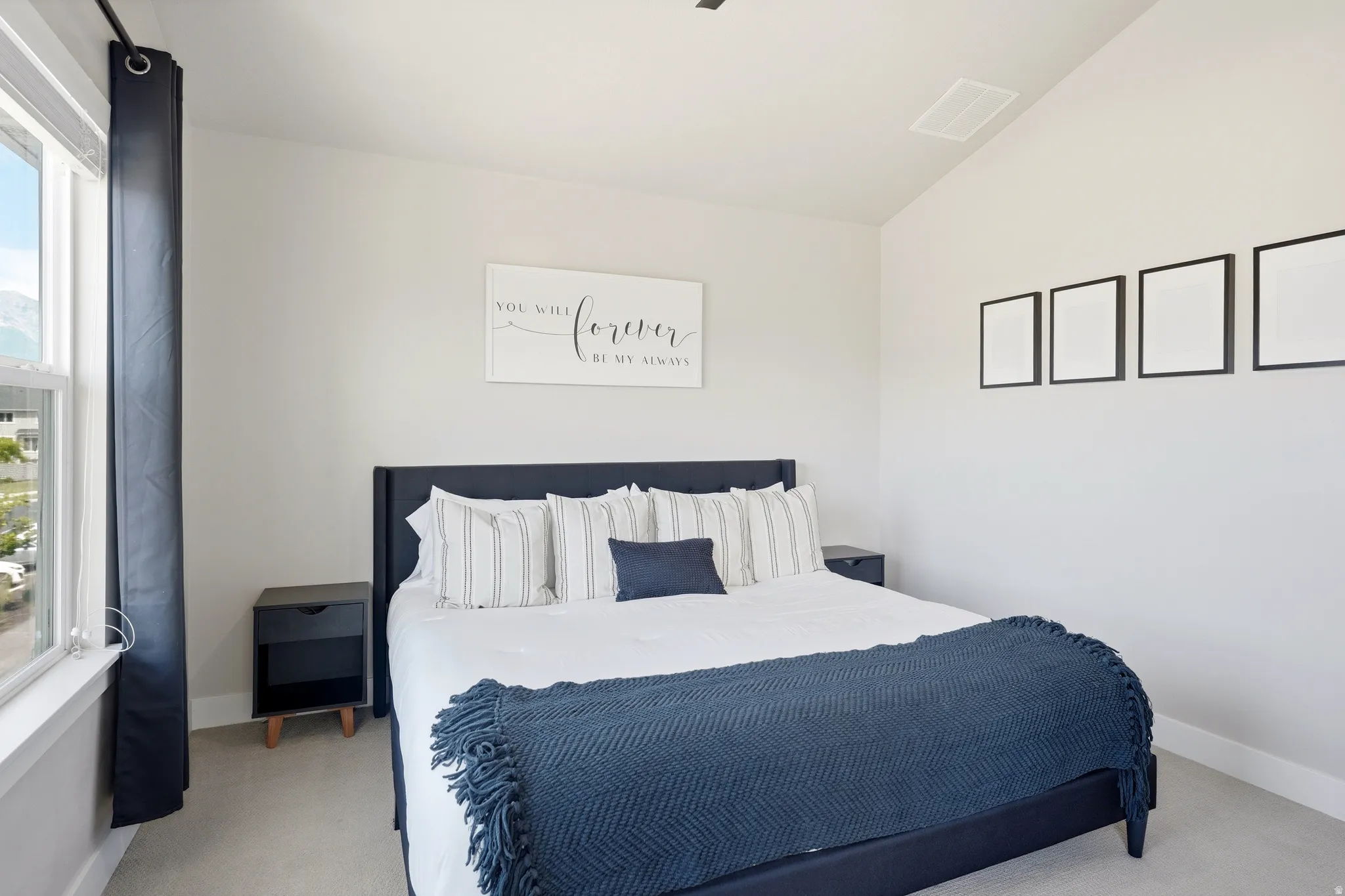 Carpeted bedroom featuring a large window, vaulted ceiling, and neutral wall tones
