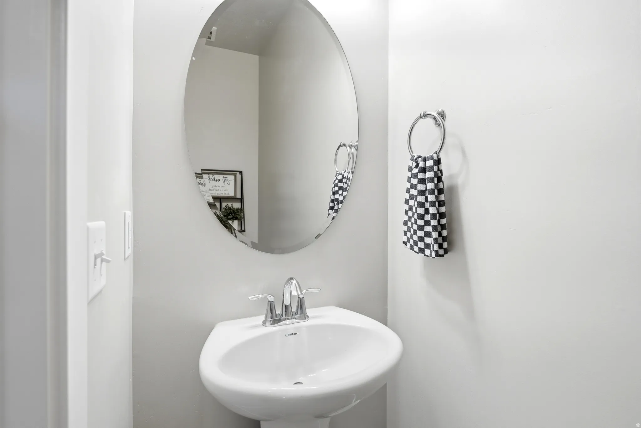 Pedestal sink with chrome faucet, complemented by an oval-shaped mirror