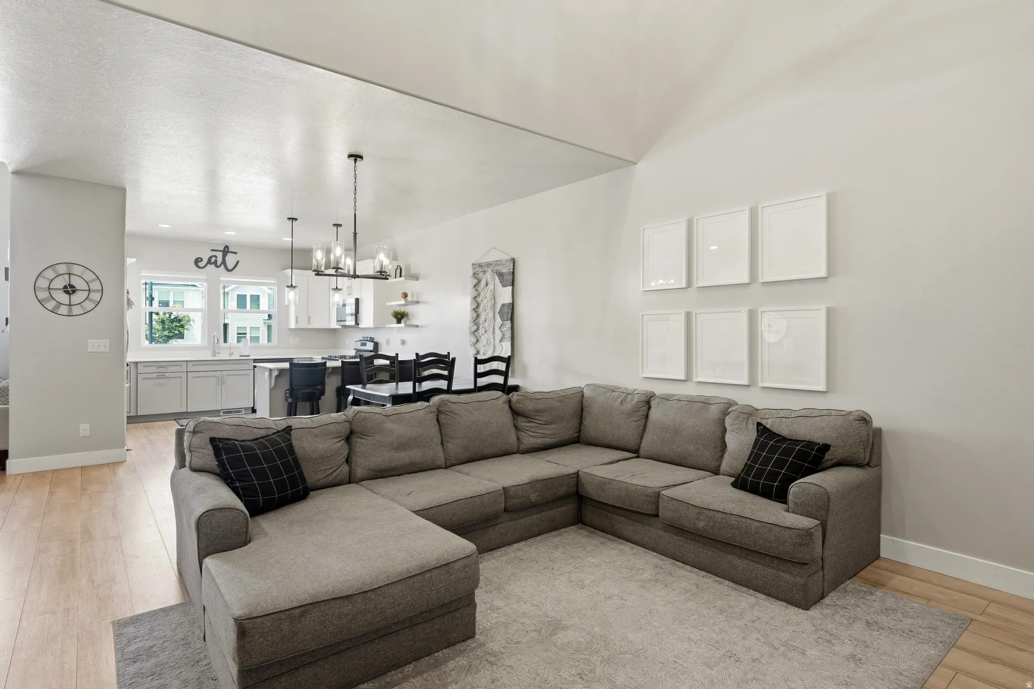 Open-concept living area featuring light wood-finish flooring, a vaulted ceiling, and white wall finishes