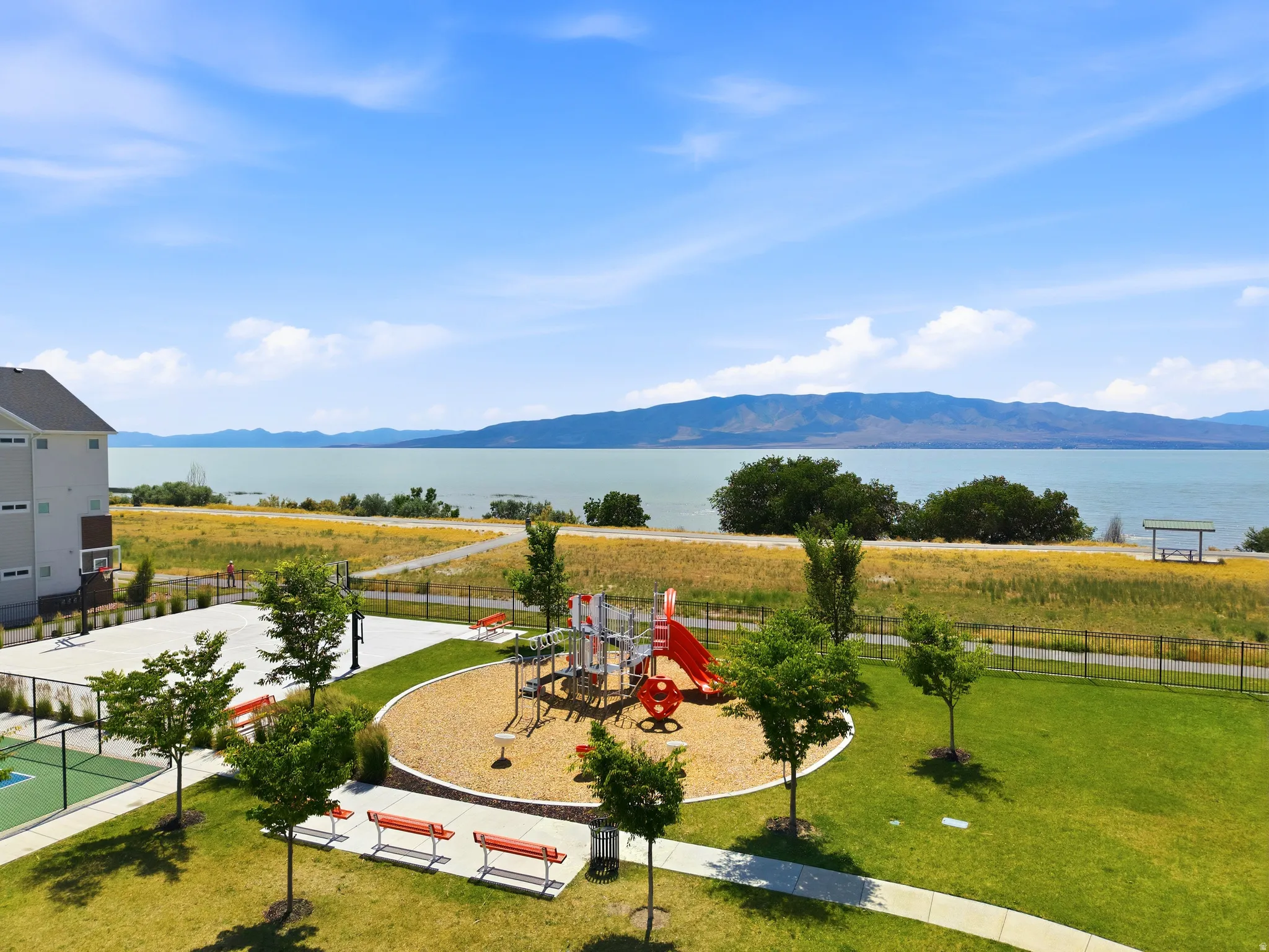 Outdoor amenities featuring a playground with a slide, a basketball court, and a green space with mature trees