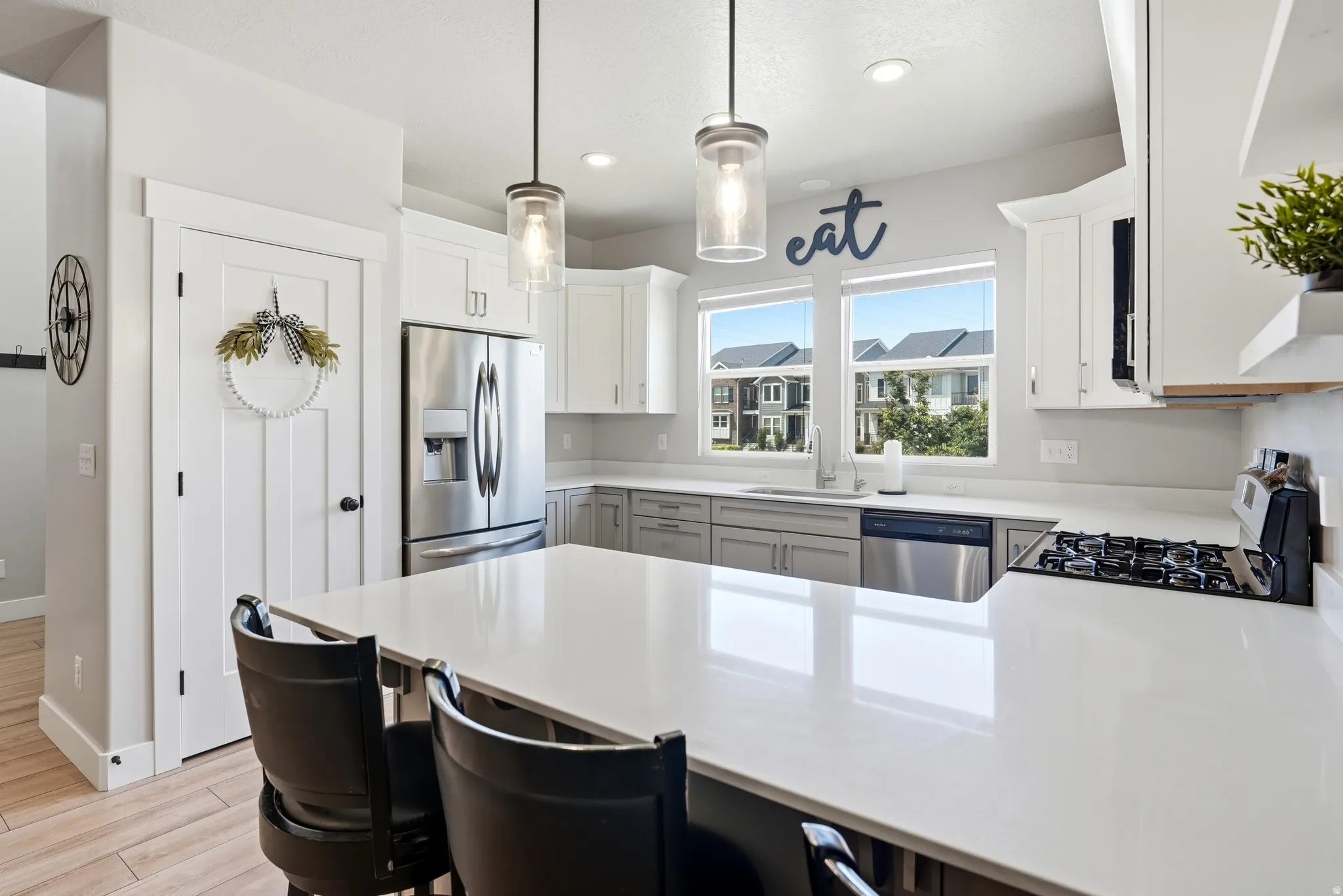 Modern kitchen featuring a large white countertop island, stainless steel appliances, a gas range, and white upper cabinetry complemented by grey lower cabinetry