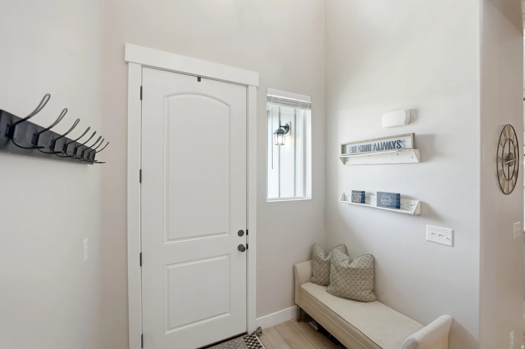 Entryway featuring a paneled door, high ceilings, a wall-mounted light fixture, and light wood-finish flooring