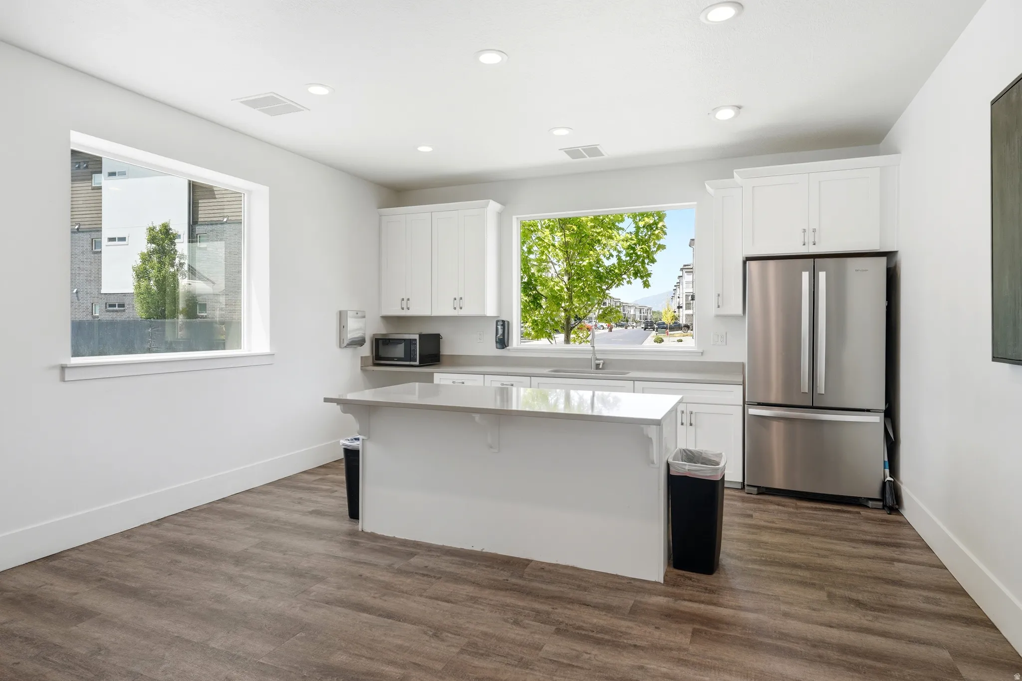 Contemporary kitchen featuring white cabinetry, stainless steel appliances, a center island with countertop, and wood-finish flooring