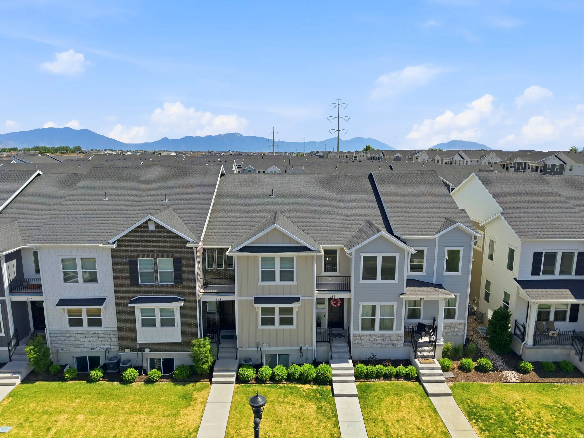 Townhome featuring a dark gray shingle roof, light gray siding, and stone accents