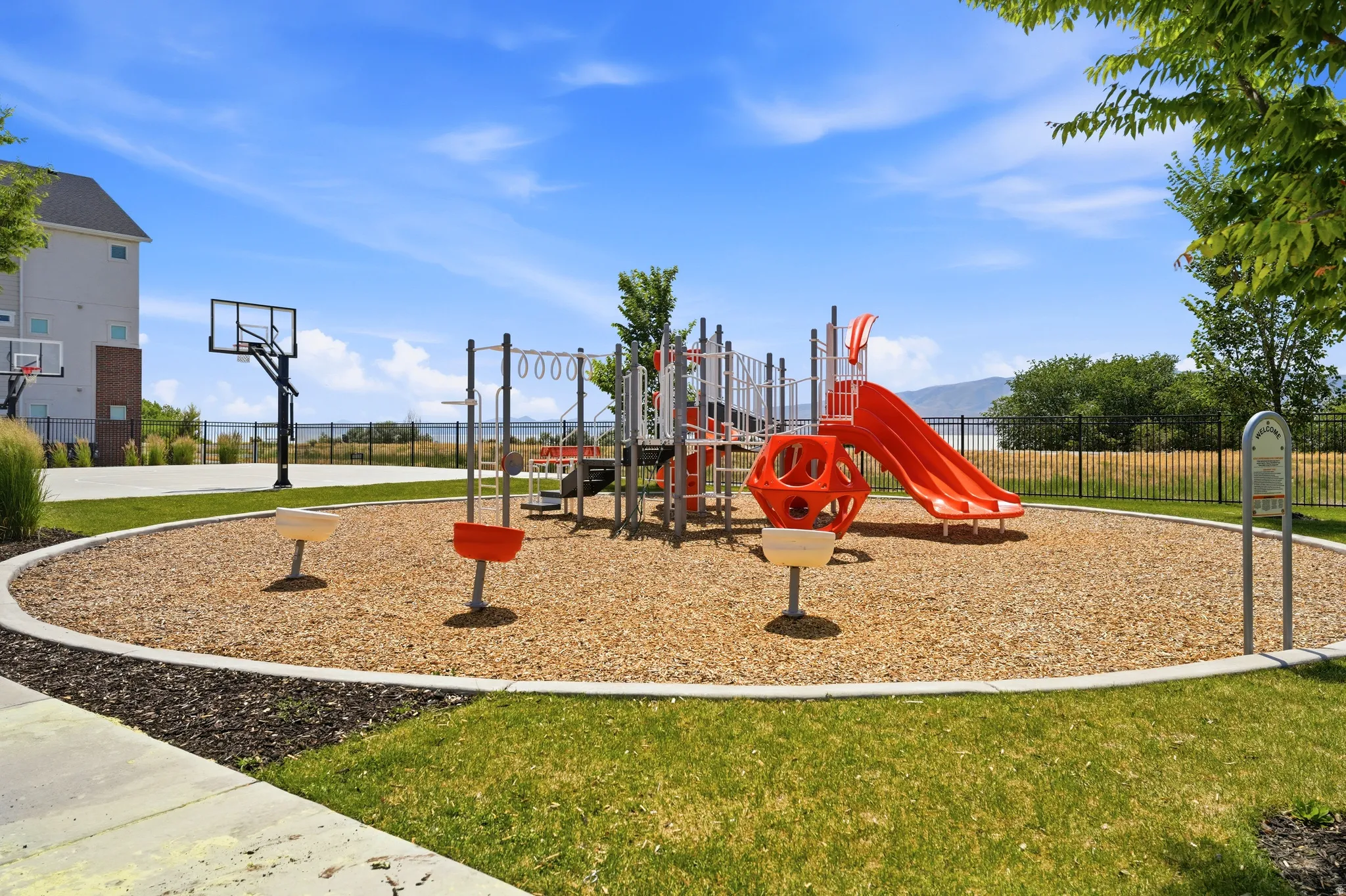 Recreational playground area featuring woodchip surfacing, red and grey play structures, and a basketball court