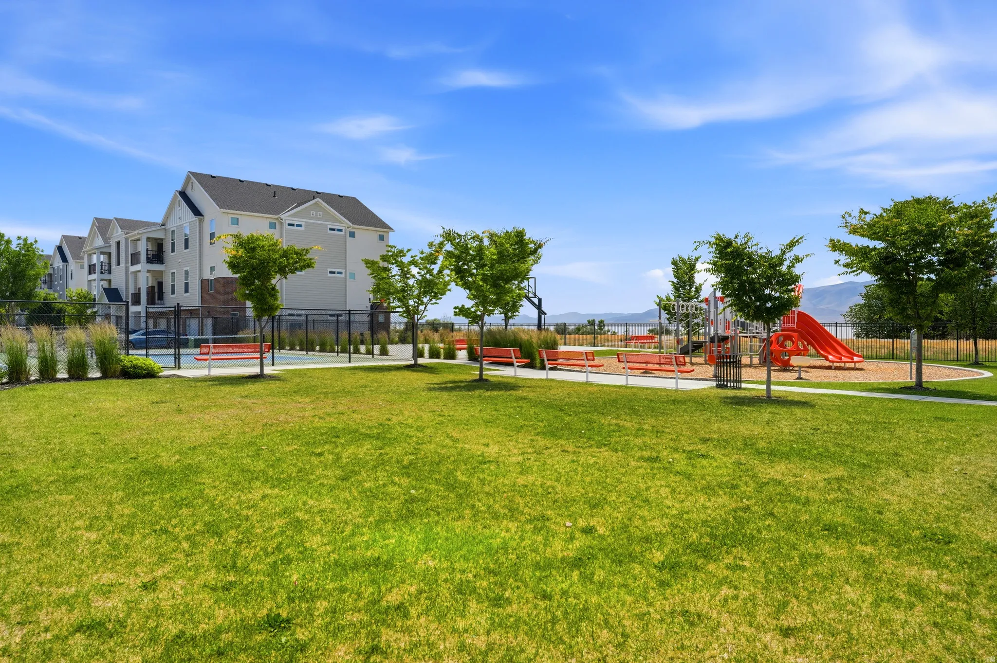 Expansive green space featuring a playground with slides and swings, alongside a sports court