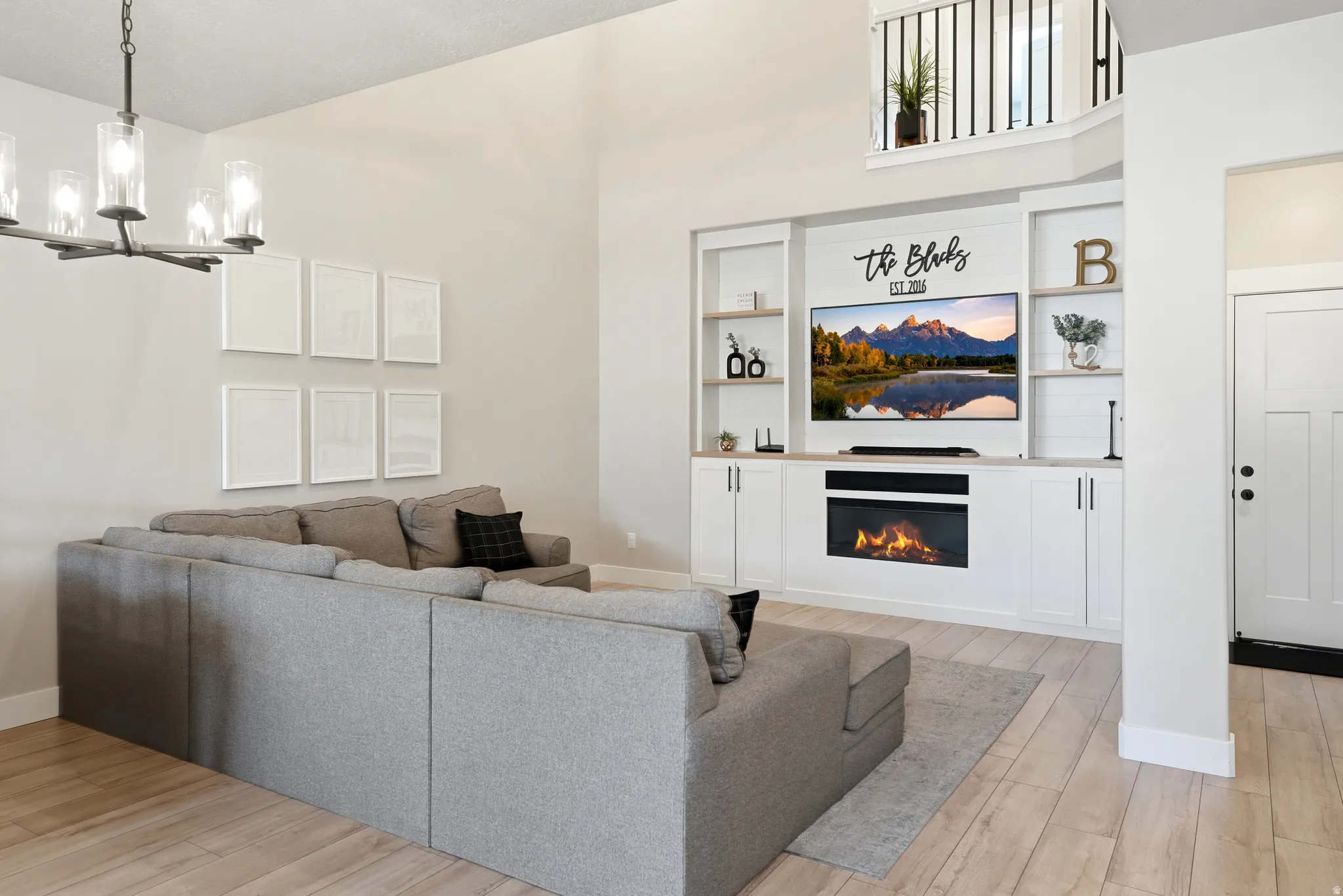 Living area featuring a floor-to-ceiling media built-in with an integrated electric fireplace, white shaker cabinetry, and open shelving